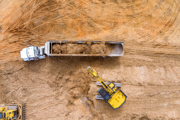 Aerial view above a excavator loading wood chopped into a dump truck to prepare land for construction site