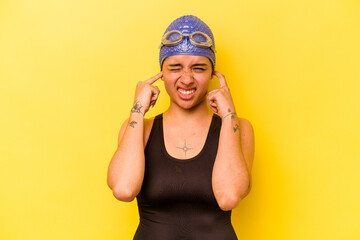 Young swimmer hispanic woman isolated on yellow background covering ears with hands.