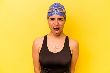Young swimmer hispanic woman isolated on yellow background screaming very angry and aggressive.