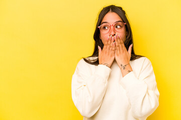 Young hispanic woman isolated on yellow background thoughtful looking to a copy space covering mouth with hand.