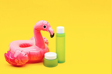 Set of green cosmetic bottle, jar and inflatable pink flamingo on yellow background. Summer collection of skin care product.