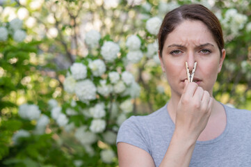 Caucasian woman with a clothespin on her nose on a walk in a blooming park. 