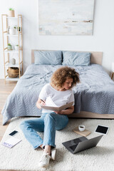 full length of copywriter working on floor in bedroom near gadgets and coffee cup.
