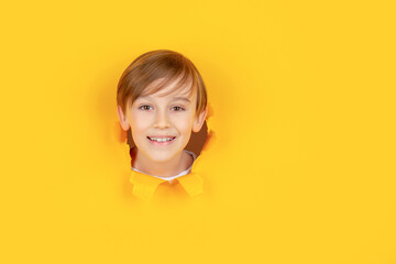 Kid with toothy smile shows face in paper hole. Positive child with toothy pleasant smile on face,...