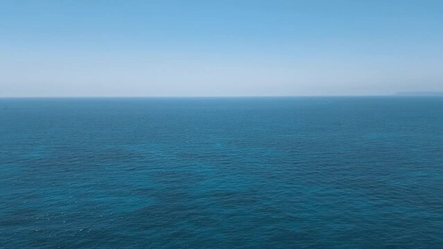 Panoramic aerial view over an expanse of the bright blue sparkling water of the Mediterranean Sea. With a long horizon and only two small boats in the distance.