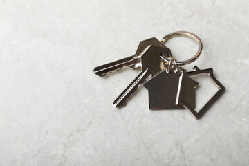 House keys with a keychain in the shape of a house.Composition on a gray marble background.Design element.Real estate and insurance concept.Place for copy.