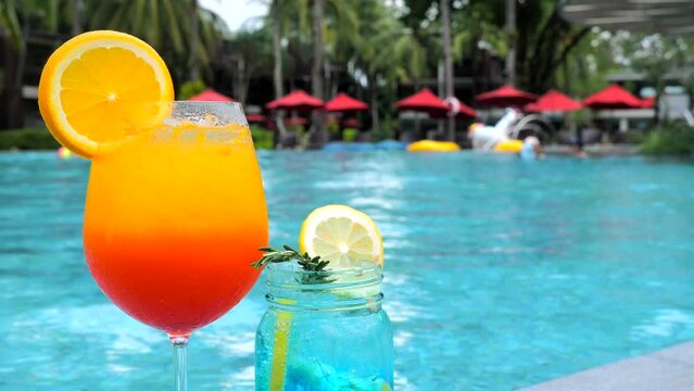Summer vacation. Two glasses of tropical iced cocktail drinks on poolside with fun peoples and sun umbrellas on background. Luxury travel, holidays concept. Phuket, Thailand.