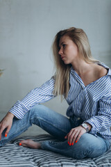 Young girl in casual relaxed pose at home. Young blonde emotional sensual woman in jeans