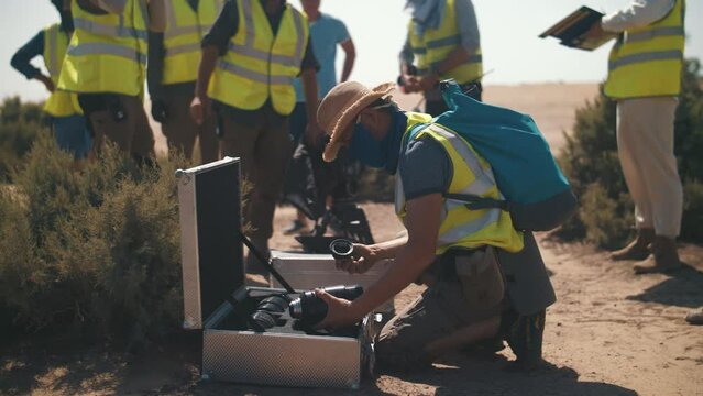 A Man On The Set Of A Film In The Desert, Wipes The Lens From The Sand.