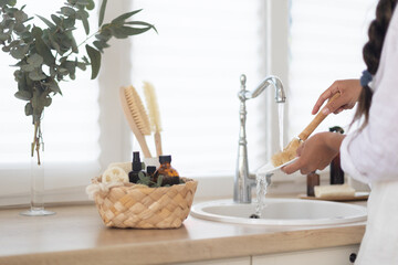 Woman washing dishes with detergent on kitchen. Eco brush with foam and basket on white bright kitchen.
