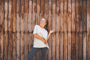 Cheerful fashion girl laughing positive pastime leisure near wooden promotional background, happy Caucaisan youngster in optical eyewear for provide eyes protection smiling at publicity area