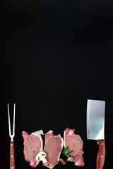 Pieces of raw roast beef meat with ingredients, meat knife and meat fork on dark background.