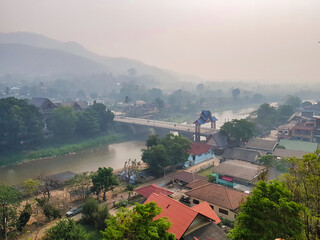 Obraz premium View from the Wat Tha Ton (Thaton) in the north of Chiang Mai province (Thailand) on a misty morning, featuring a bridge with a traditional gate, the river Kok, a village and hills. 