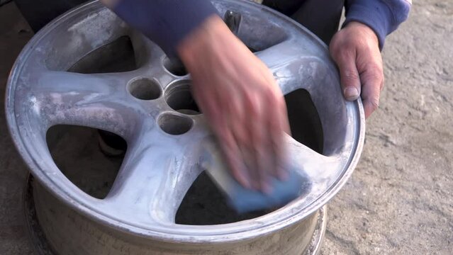 A man protects the wheel from old paint with sandpaper. Preparing the wheel for painting. Car wheel. Service worker. Garage workshop. Works on the street.