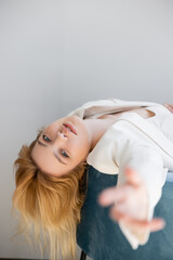 Naklejka premium Young woman in jacket looking at camera on armchair near grey wall.