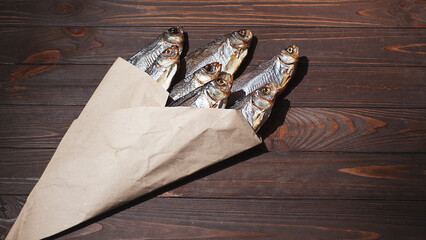 dried smoked fish smelt, on a dark wooden board, in craft paper, dark light, top view