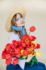 A young woman holds a bouquet of red tulips in her hands. The concept of March 8, Valentine's Day. A wonderful gift for a girl. Spring portrait of a woman in a straw hat.