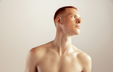 Portrait of young red-haired freckled man posing shirtless isolated over grey studio background.