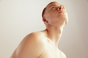 Portrait of young red-haired man posing shirtless, looking upwards isolated over grey studio...