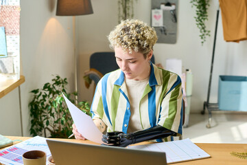 Young female economist with arm prosthesis working with financial documents while sitting by...