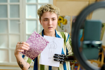 Young creative female fashion designer showing drawing of new model for seasonal collection to...