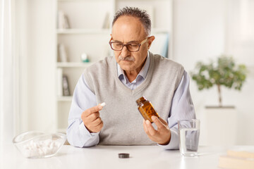 Mature man sitting at home and taking a pill