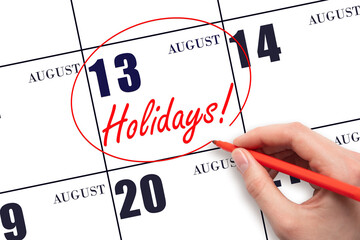 Hand drawing a red circle and writing the text Holidays on the calendar date 13 August. Important date.