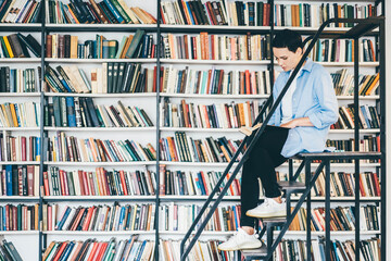 Young woman reading a book in front of bookshelves. Education concept.