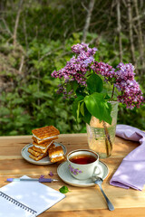 Tea party with Viennese waffles and a branch of lilac and an open empty notebook for writing on a wooden table against the background of the garden on a sunny day. The concept of a new life.