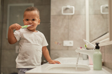 Portrait of black toddler boy brushing teeth in bathroom and looking at camera, copy space
