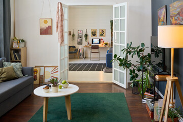 Interior of spacious living room with open door to another large room with workplace, couch,...