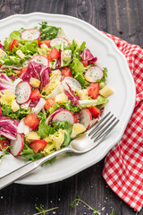 Fresh salad with mixed greens radish cheese and tomato in a plate on wooden background. Italian Mediterranean or Greek cuisine.