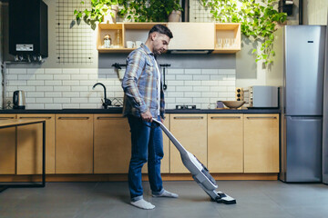 A young man cleans the apartment with a vacuum cleaner.