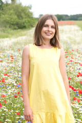 Fototapeta na wymiar a beautiful young blonde woman in a yellow dress stands among a flowering field
