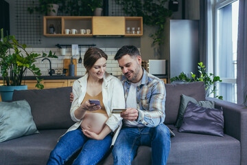 Online shopping. Young family, pregnant woman and man make an online purchase from the phone, holding a credit card. Sitting at home on the couch.