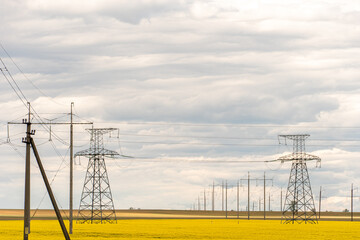 Power line in rape field. A line of electric poles with cables of electricity in a rape field. The concept of clean and renewable energy. Agriculture in an ecologically clean place