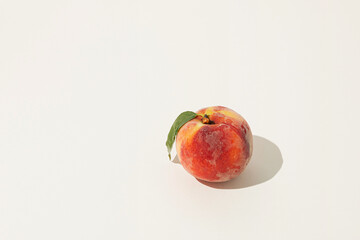 Minimal raw food concept made of sunlit fresh ripe juicy peach with green leaf on isolated pastel beige background. Natural summer fruit pattern. Sun and shadows. Organic agriculture production idea.