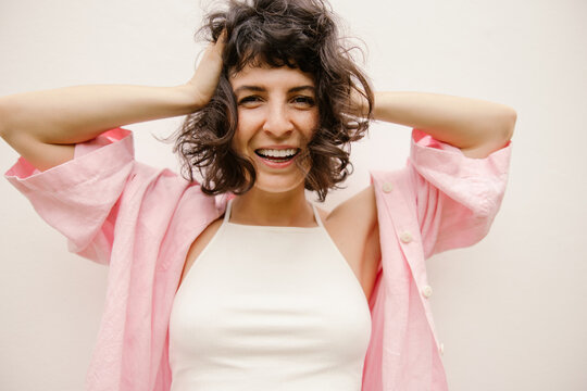 Happy young caucasian woman looking at camera holding head with hands on white background. Brunette girl with short wavy hair wears casual summer clothes. Mood, lifestyle, concept.