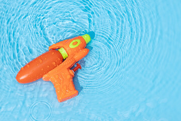 Water gun toy on blue water surface with rippled waves. Fun, leisure summertime background. Copy...