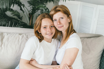Mother and teenage daughter hugging at home on the couch. 