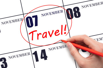 Hand drawing a red circle and writing the text TRAVEL on the calendar date 7 November. Travel planning.