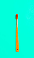 Orange plastic toothbrush on mint green background, close up