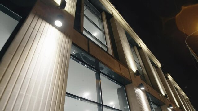 Powerful led lamps illuminate facade of contemporary car dealership building on snowy street of night city closeup combined shot