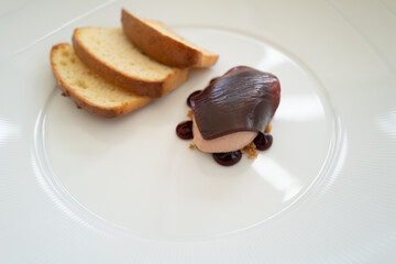 Shallow focus on the jelly on top of a quenelle spoon serving of pate on a plate with toast.