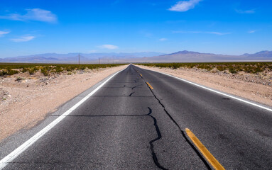 Asphalt road leading through steaming hot landscape of Death Valley National Park, California, USA. Super hot sunny day in the desert of the southwest. Vast land of dirt and dust.