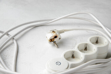 Burnt electric extension cord plug after a short circuit, faulty electrical appliance, gray concrete background, close-up.