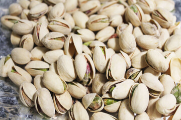 Unpeeled pistachios in a brown shell lie in a pile on a silver foil, close-up, top view. Snack for beer. Salted pistachios.