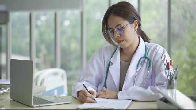 Attractive Female Doctor working with laptop computer and writing on paperwork,  female doctor make online video call consult patient on laptop, Medicine and health care concept