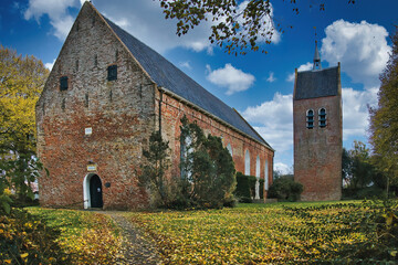 The 12-th century church in the village of Baflo, province of Groningen, the Netherlands, on an autumn day, with fallen leaves in the foreground.
