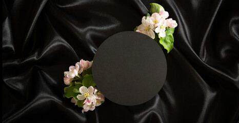 Empty geometric platform podium stand for cosmetics product presentation and spring blooming tree branches with white flowers on elegant black silk satin fabric background. Top view